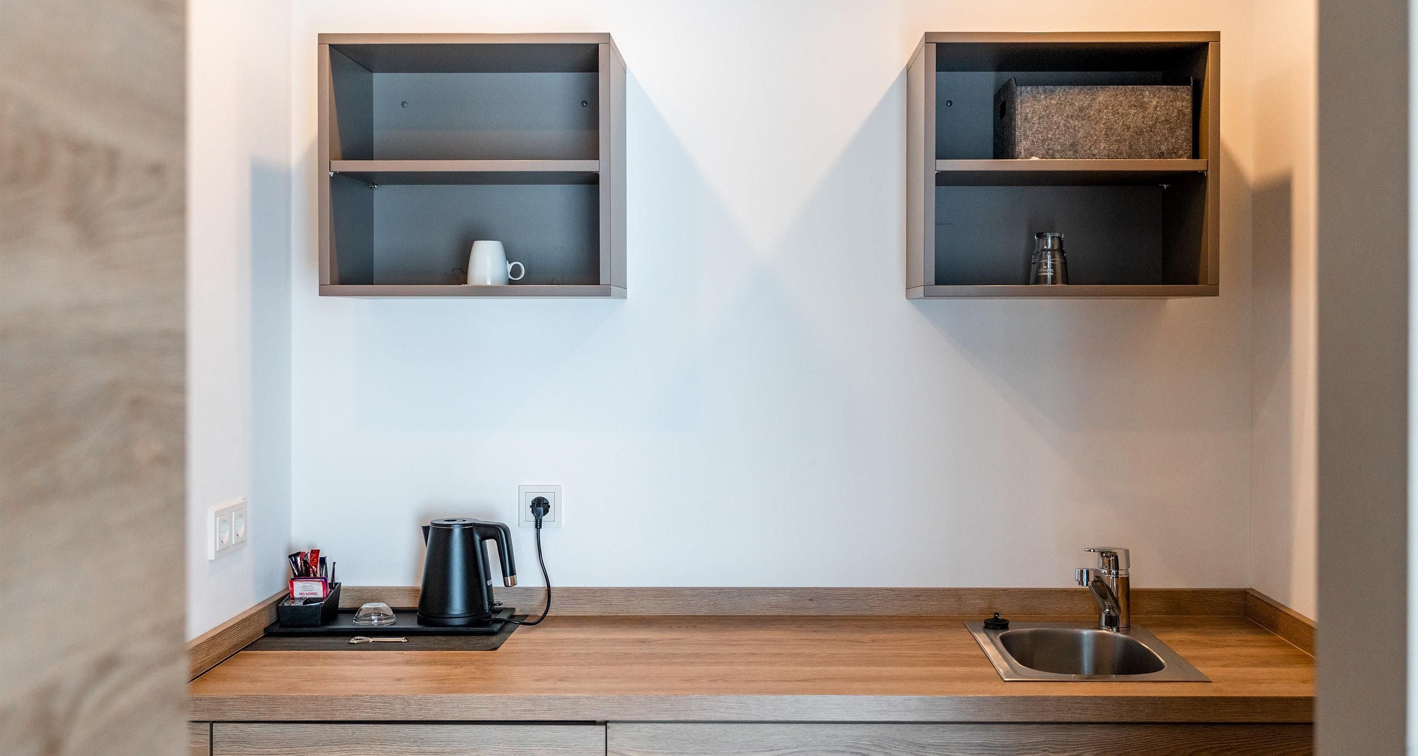 Eine moderne Küche mit einer Holzausziehtheke, einer Kaffeemaschine, einem Wasserkocher und einem Spülbecken.
