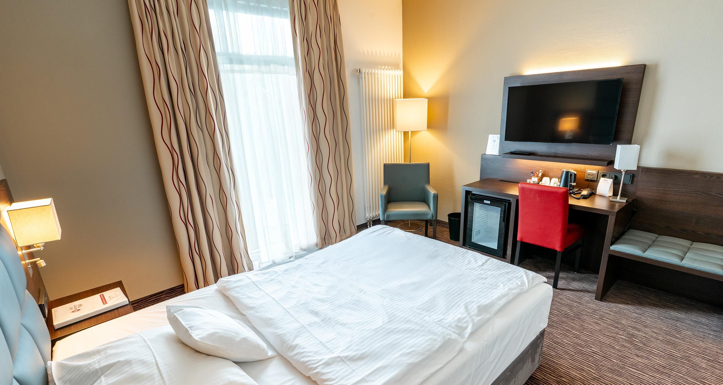 Ein Hotelzimmer mit Bett, Schreibtisch, Fernseher, Stuhl und kleinem Kühlschrank.