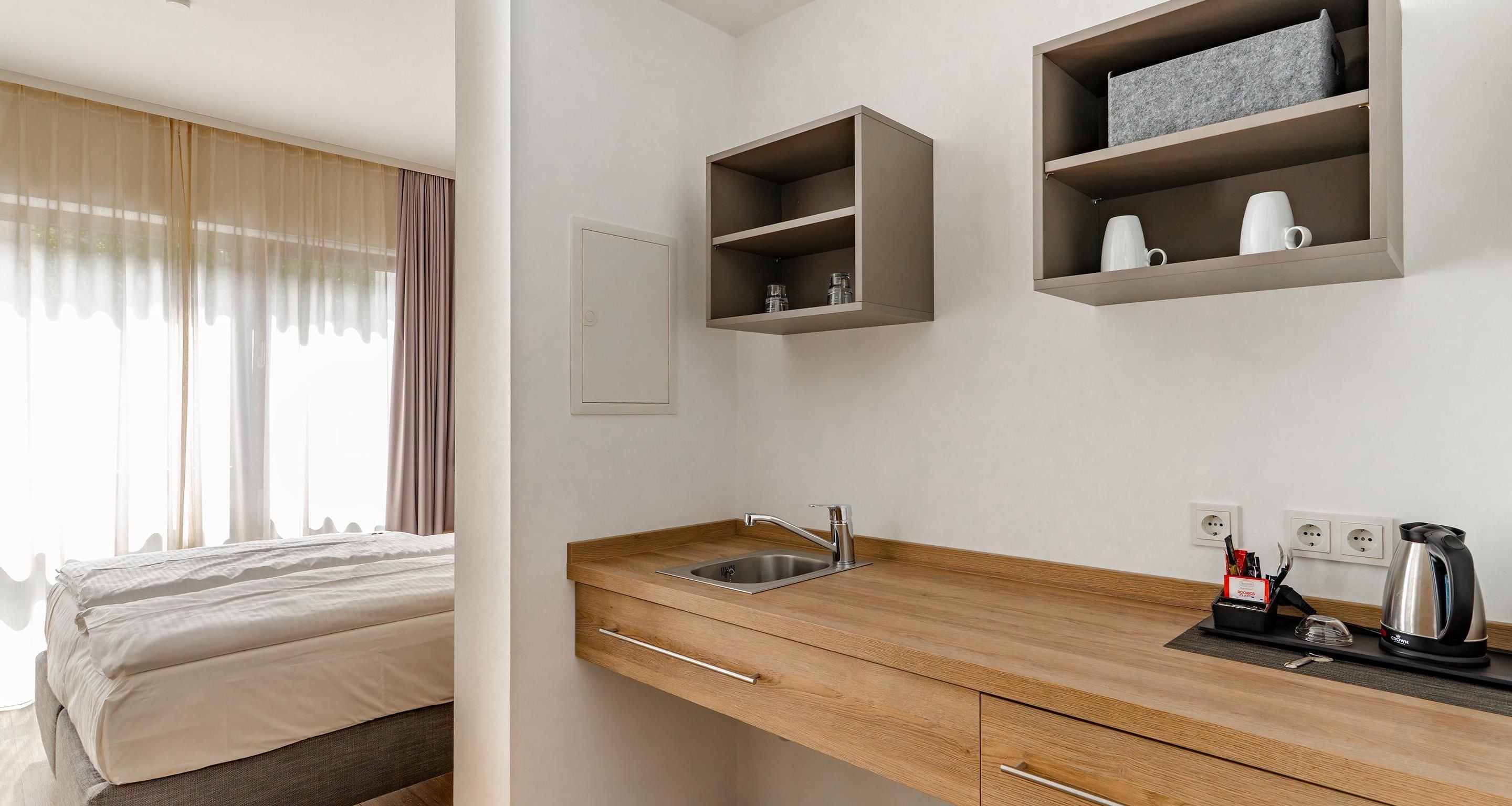 Ein modernes Hotelzimmer mit einem Bett, einer Holz-Kochnische und integrierten Regalen.