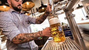 Eine Person schwenkt Bier in ein Glas in einer Bar mit einer Metallgitter-Bar und hängenden Lichtern im Hintergrund.