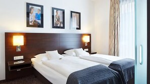 Une chambre d’hôtel avec deux lits simples, une tête de lit en bois, des lampes de chevet et des tableaux encadrés au mur.