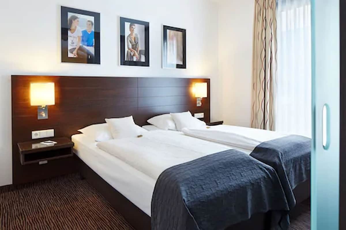 Quarto de hotel com duas camas de solteiro, cabeceira de madeira, abajures e quadros nas paredes.