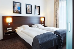 Une chambre d’hôtel avec deux lits simples, une tête de lit en bois, des lampes de chevet et des tableaux encadrés au mur.