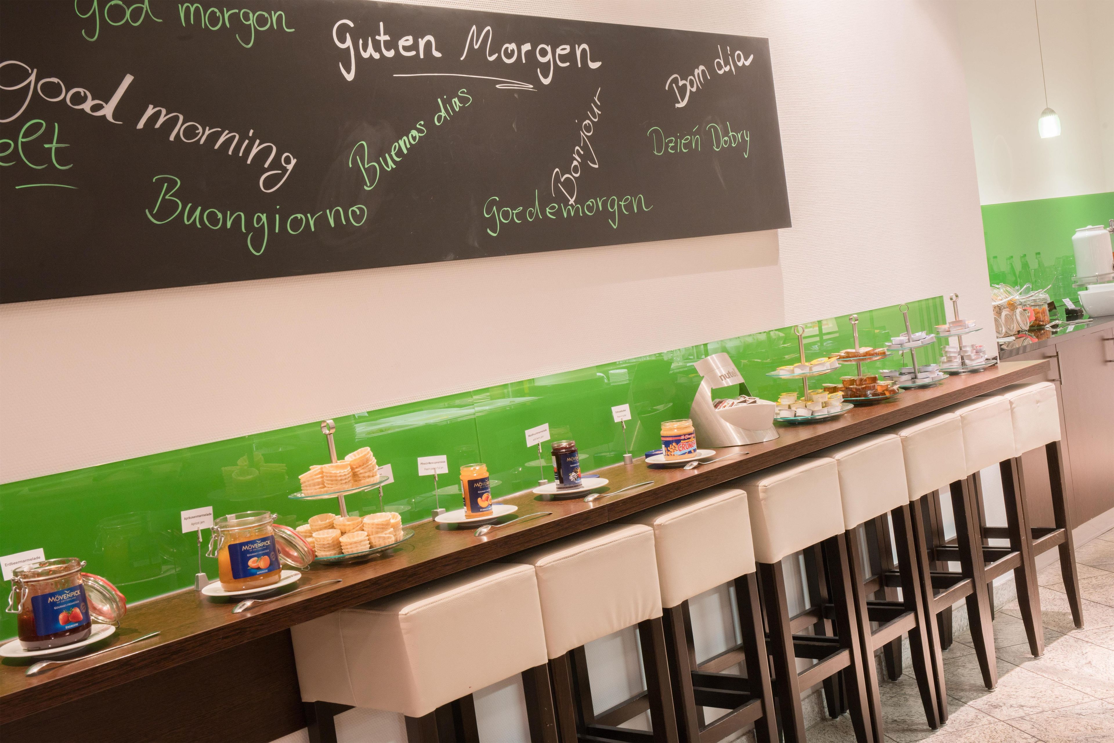 A breakfast buffet with a variety of food items and a chalkboard with greetings in multiple languages.