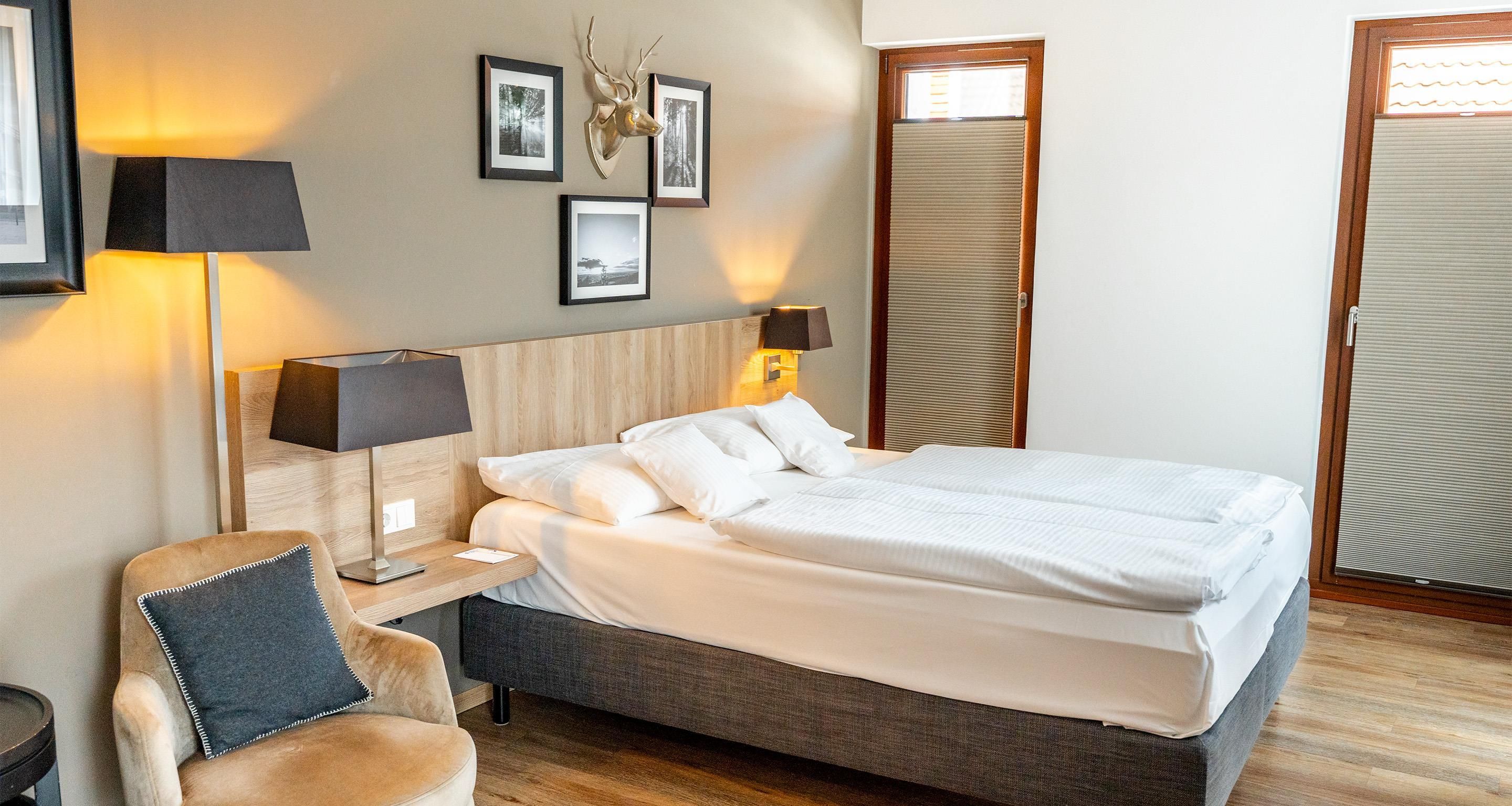 Une chambre d’hôtel bien rangée, avec un lit, des lampes de chevet, une chaise et des tableaux encadrés accrochés au mur.