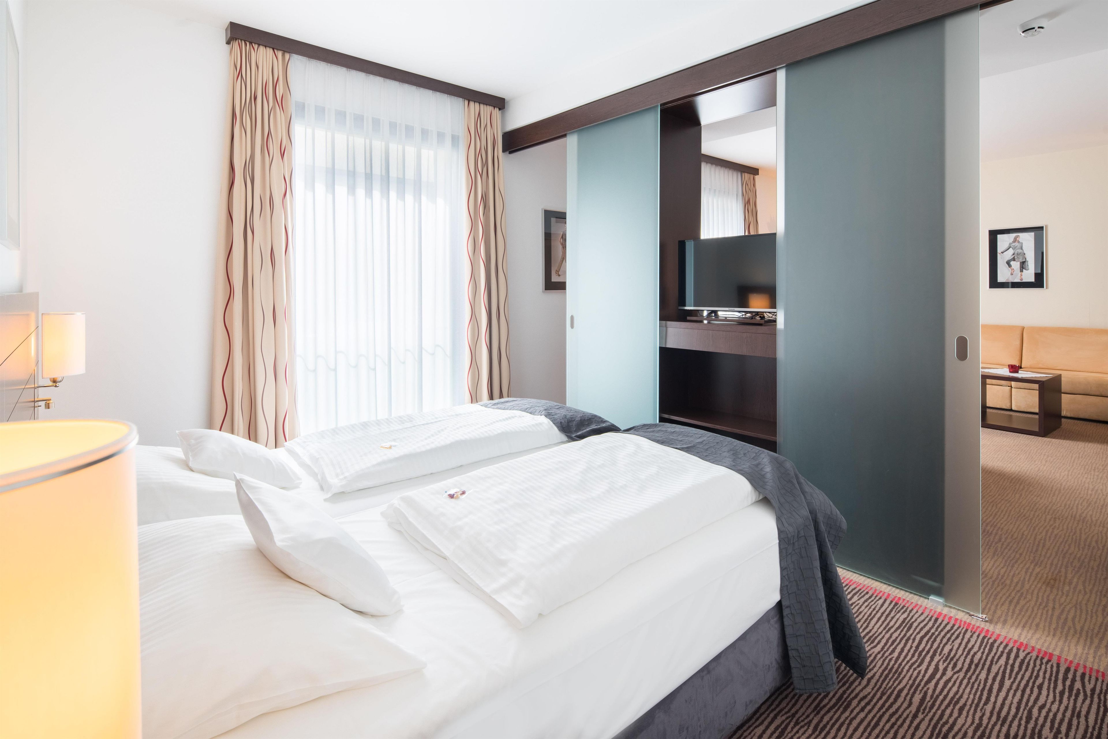 A hotel room with a bed, a desk, a television, and a bathroom visible through an open door.