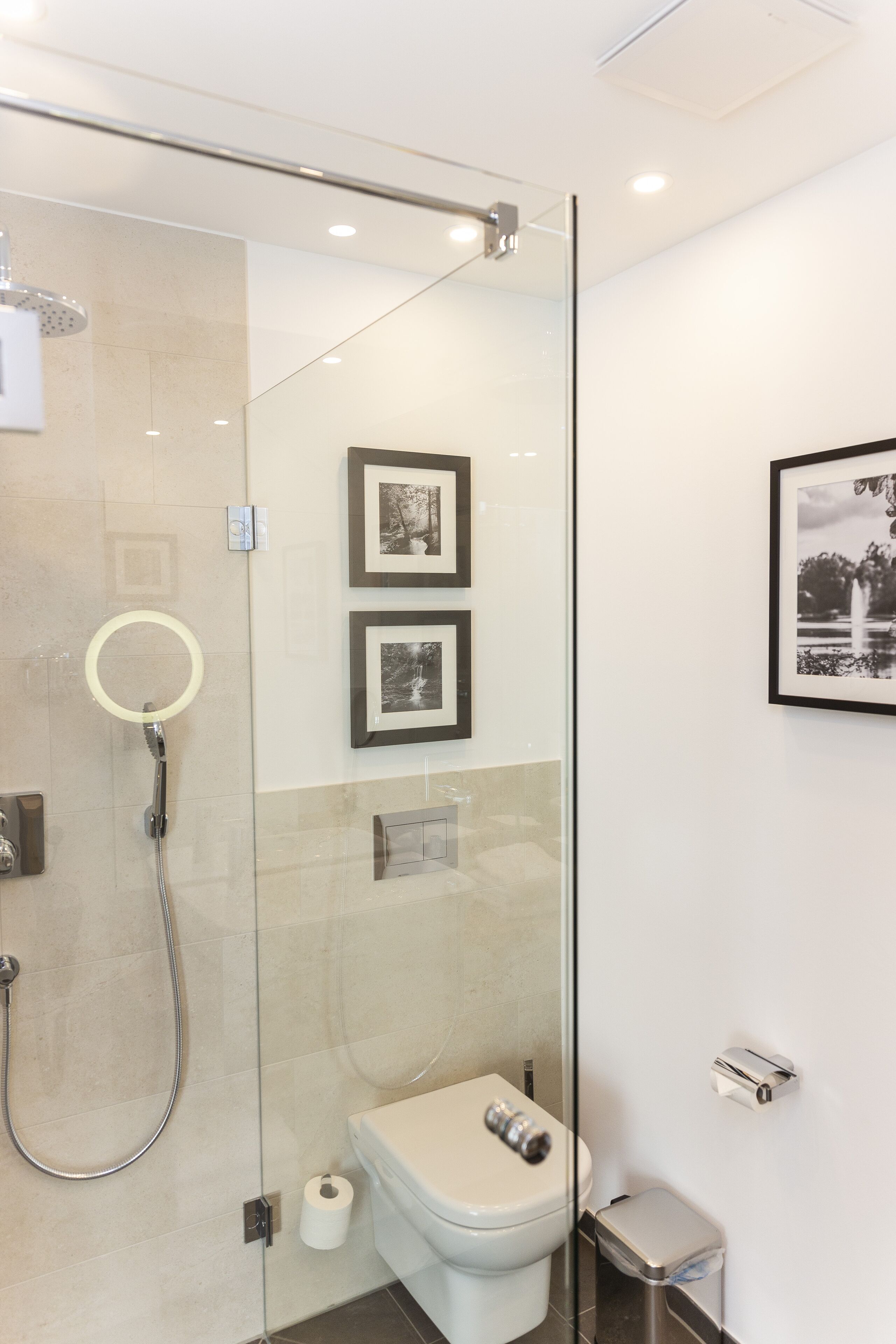 A modern bathroom with a glass shower enclosure, a toilet, and framed pictures on the wall.