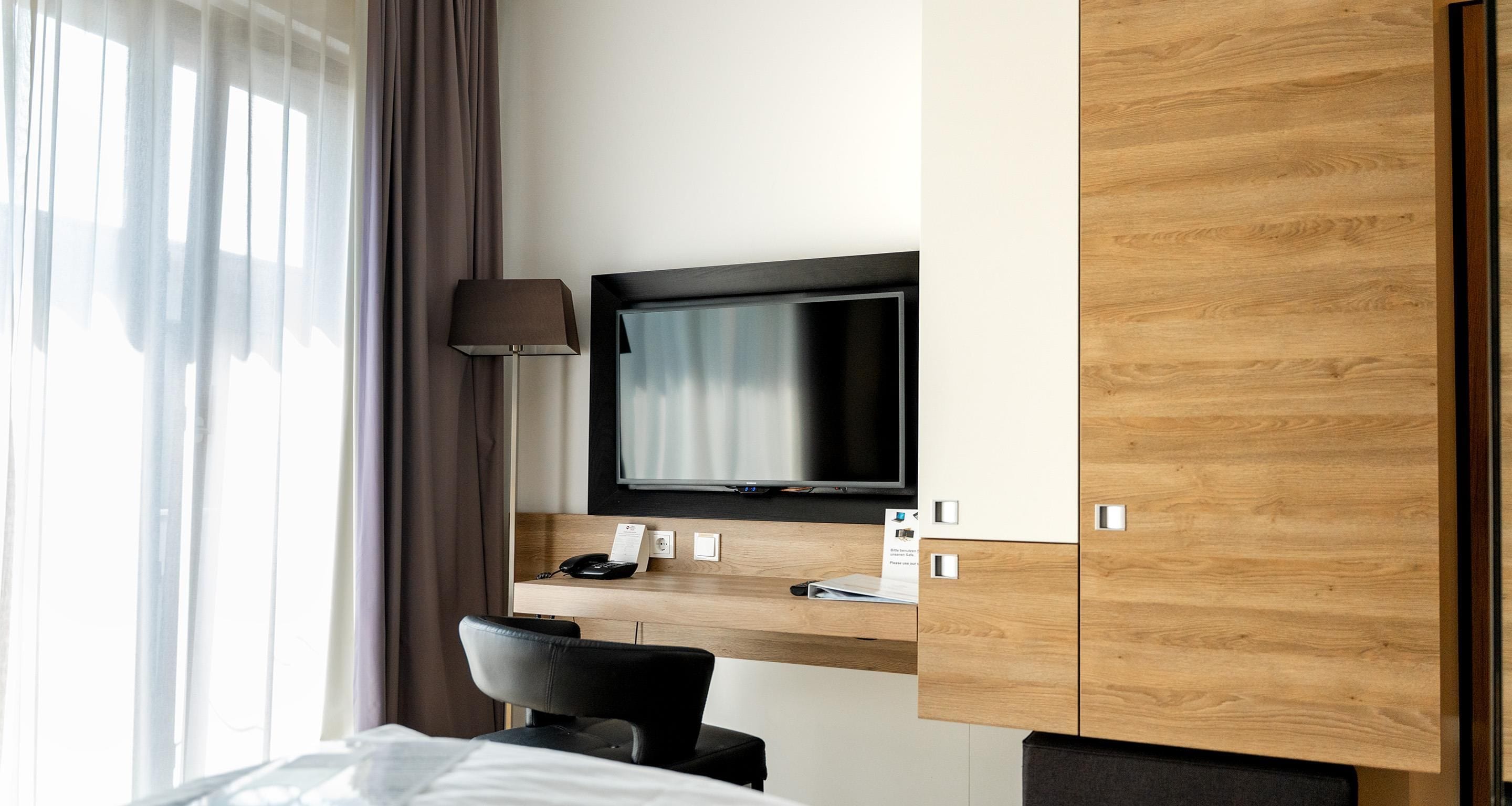 Habitació d'hotel amb llit, escriptori amb televisió de pantalla plana, telèfon i làmpada.