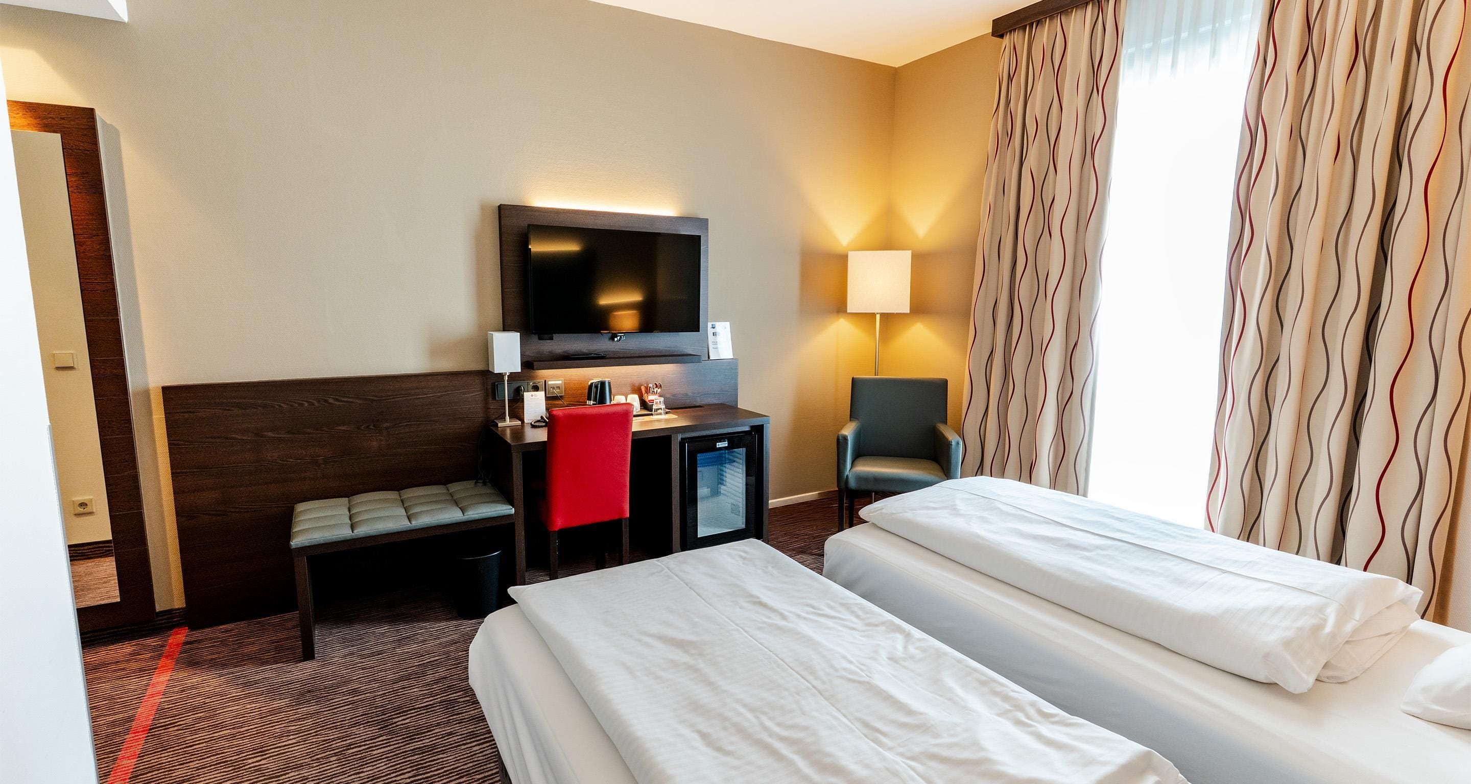 A hotel room with two beds, a desk with a television, a chair, and a lamp.