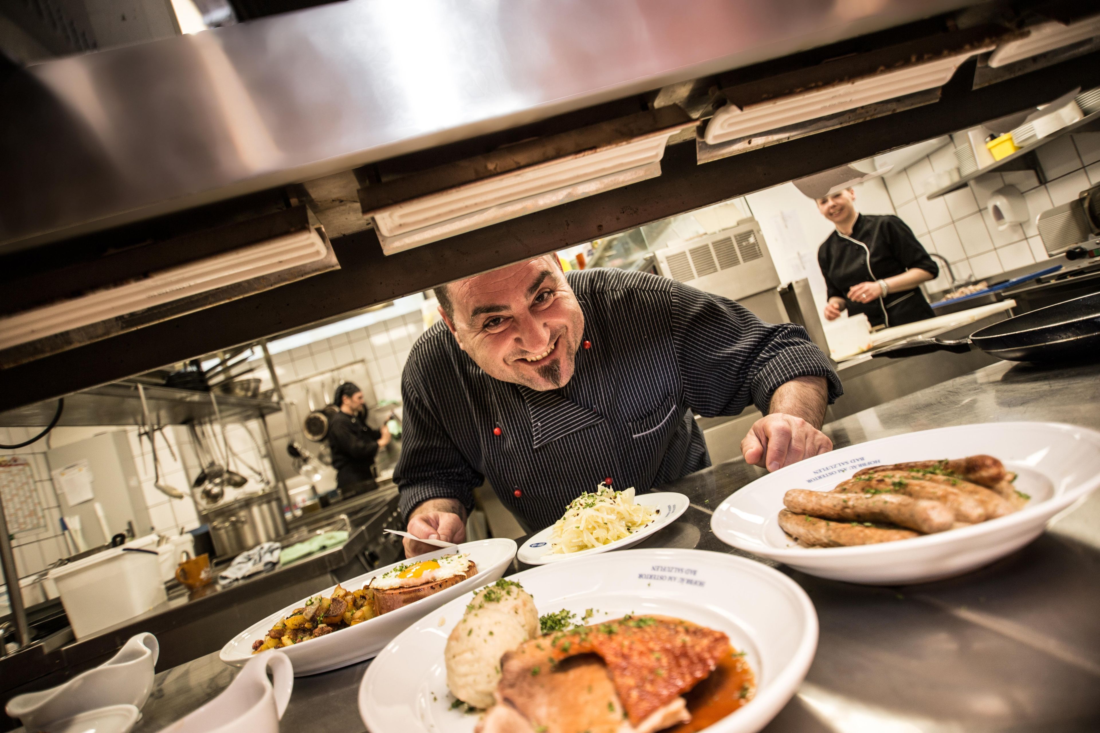 A chef in a kitchen with various dishes on plates, including what appears to be a fish dish and a potato dish.