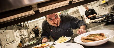 A chef in a kitchen with various dishes on plates, including what appears to be a fish dish and a potato dish.