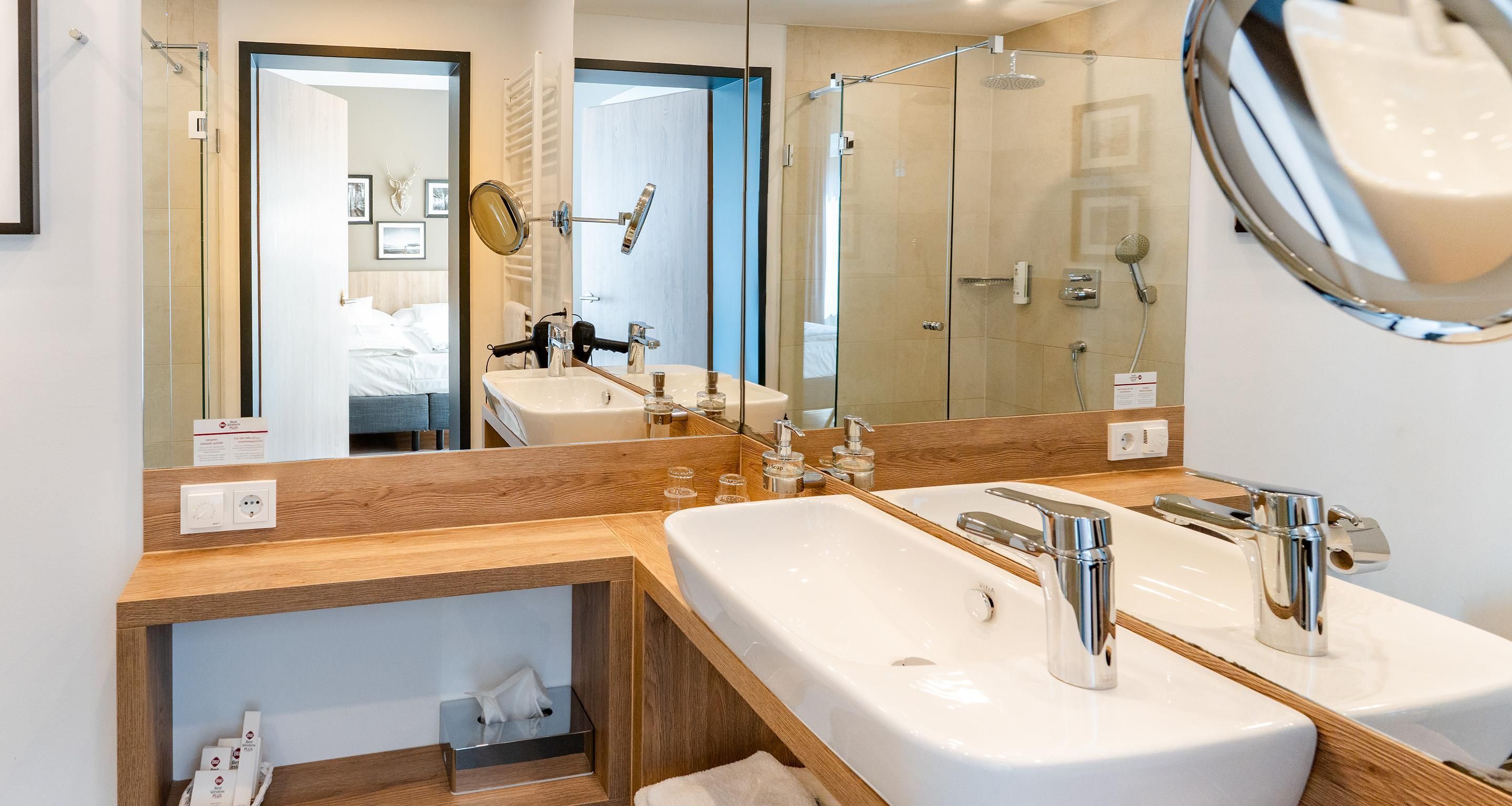 Ein modernes Badezimmer mit großem Spiegel, zwei Waschbecken, einer Duschkabine und einem Holzkosmetikschrank.