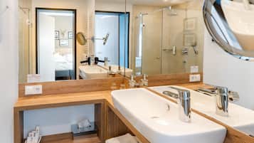 A modern bathroom with a large mirror, two sinks, a shower area, and a wooden vanity.