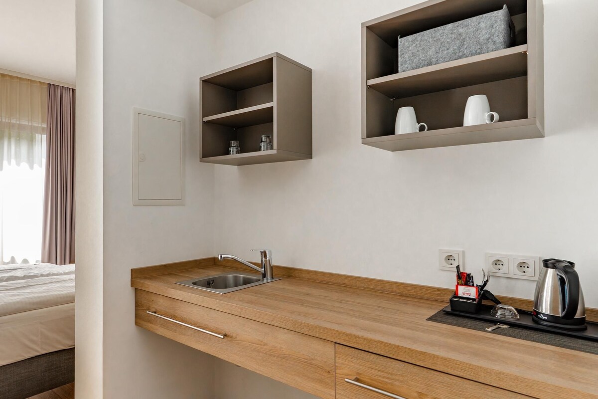 Une chambre d’hôtel moderne équipée d’un lit, d’une petite cuisine en bois et d’étagères intégrées.