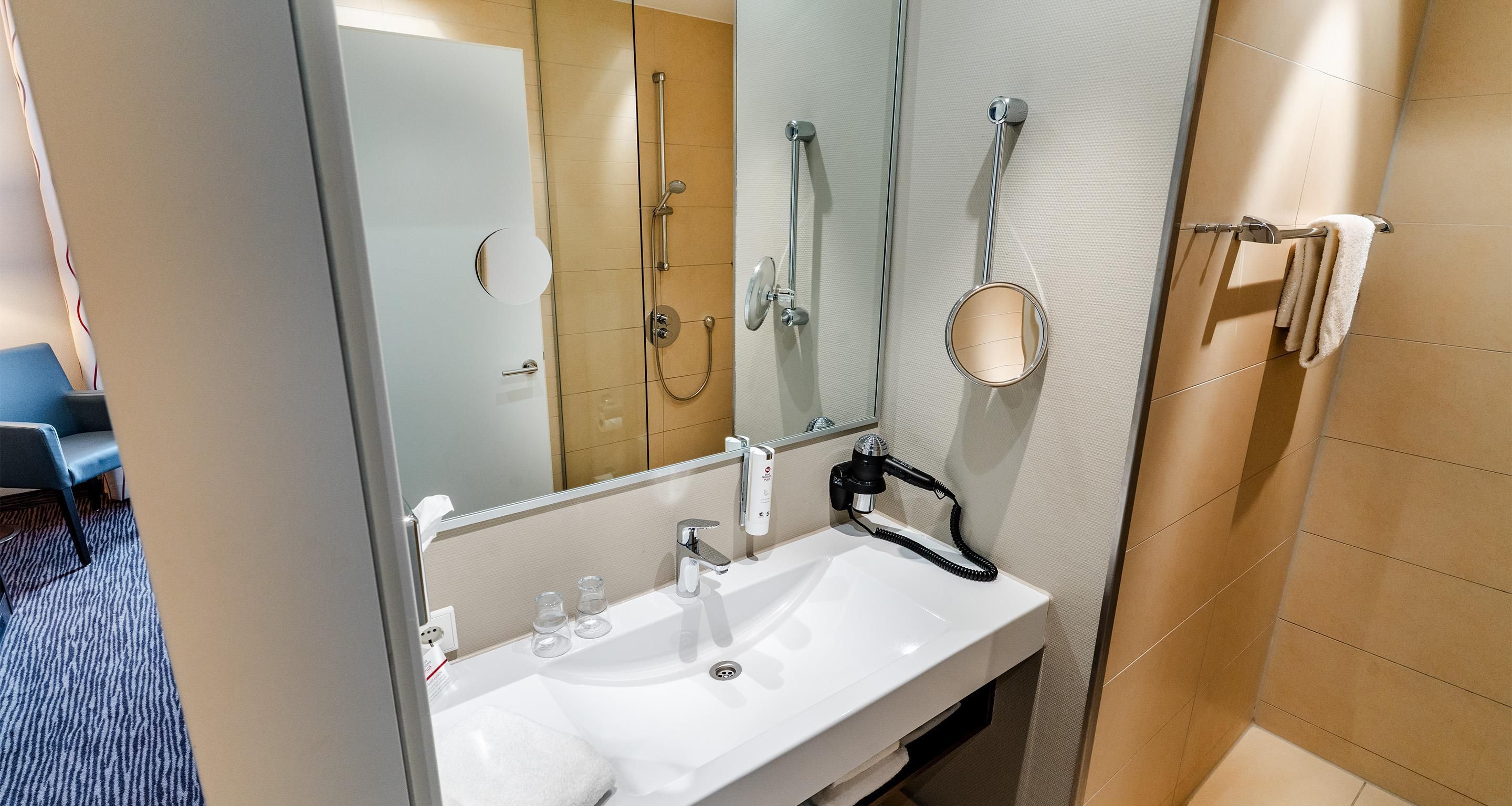 Ein modernes Badezimmer mit einem weißen Waschbecken, einer Handbrause, einem Handtuchhalter und einem Spiegel.