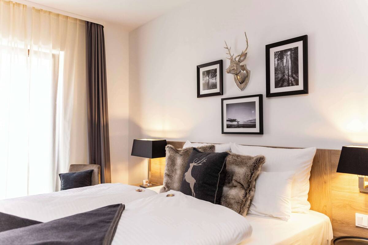 Une chambre d’hôtel avec un grand lit, deux tables de chevet avec des lampes, une décoration murale représentant une tête de cerf et trois tableaux encadrés.