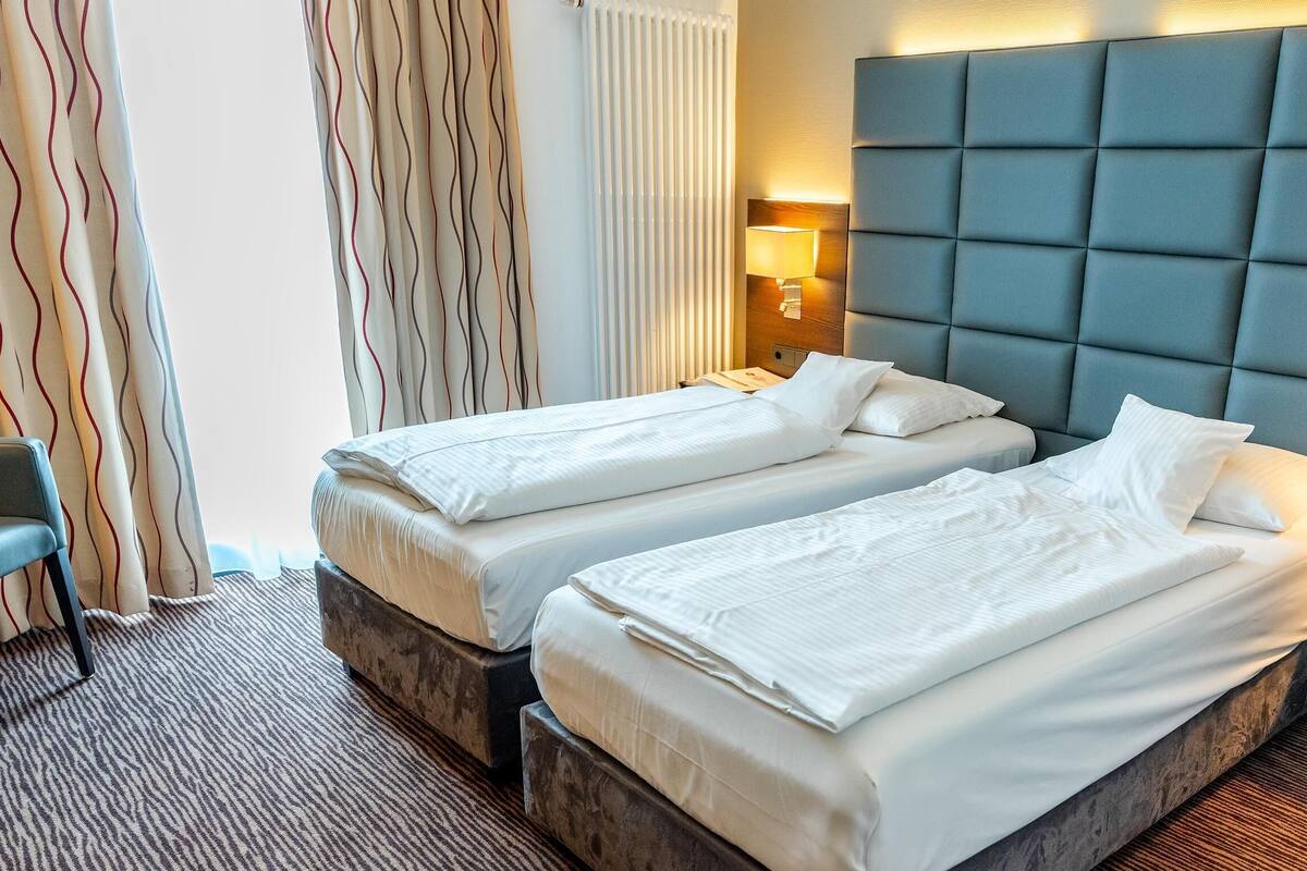 Une chambre d’hôtel avec deux lits, une grande tête de lit rembourrée, des lampes de chevet et un sol recouvert de moquette.