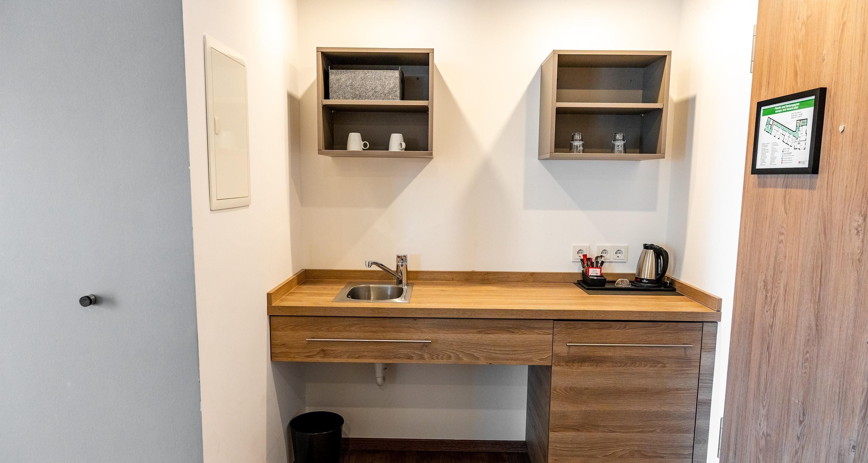 A compact kitchenette with a sink, wooden countertop, and two shelves above it.