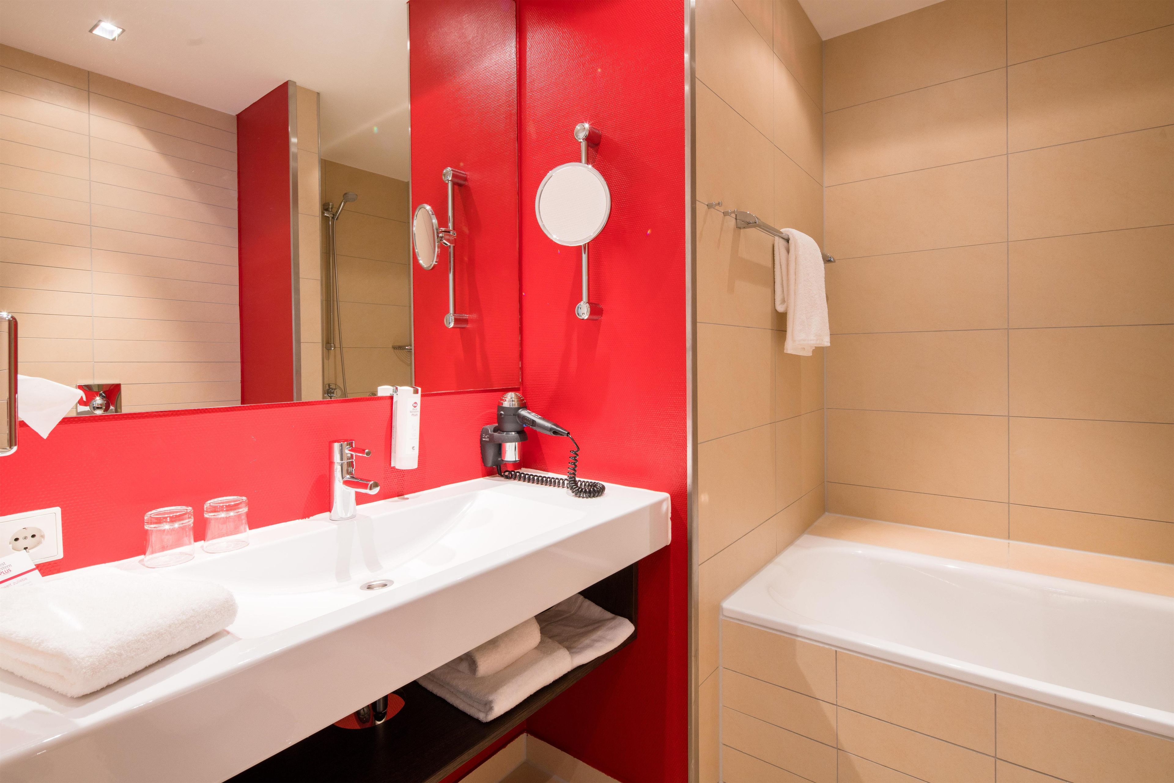 Un baño con un lavamanos blanco, un espejo, una pared de acento roja, una ducha y una bañera.