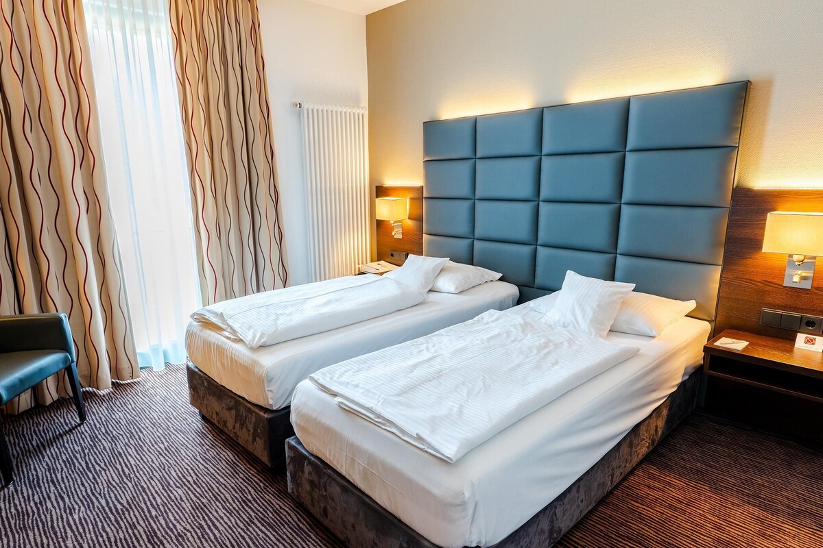 Een hotelkamer met twee bedden, een bureau, een stoel en een raam met gordijnen.