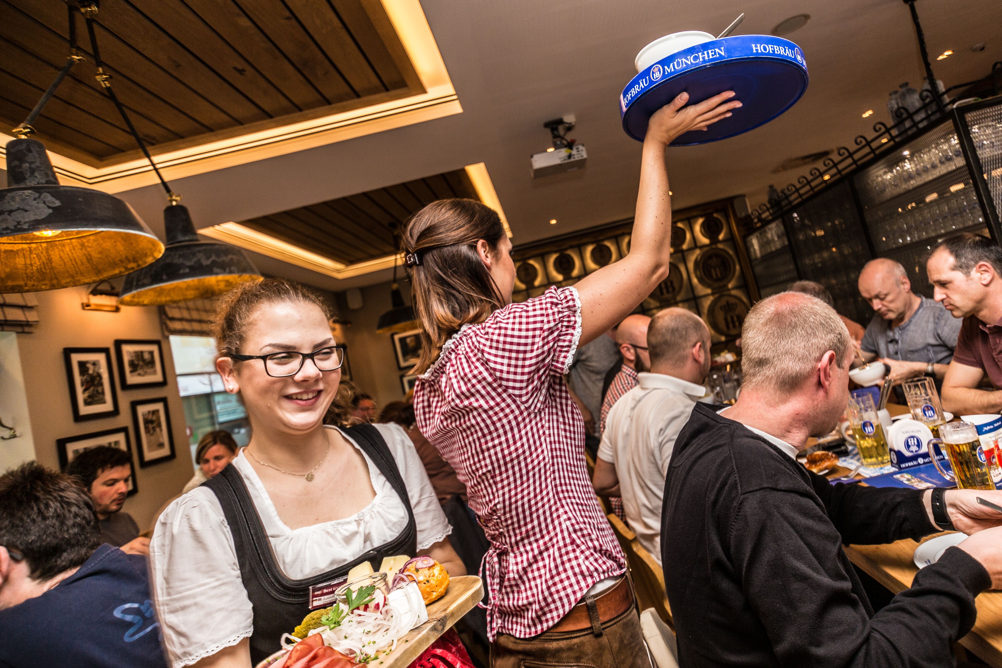 A woman serving food to a group of people in a restaurant with wooden ceiling and pendant lighting.