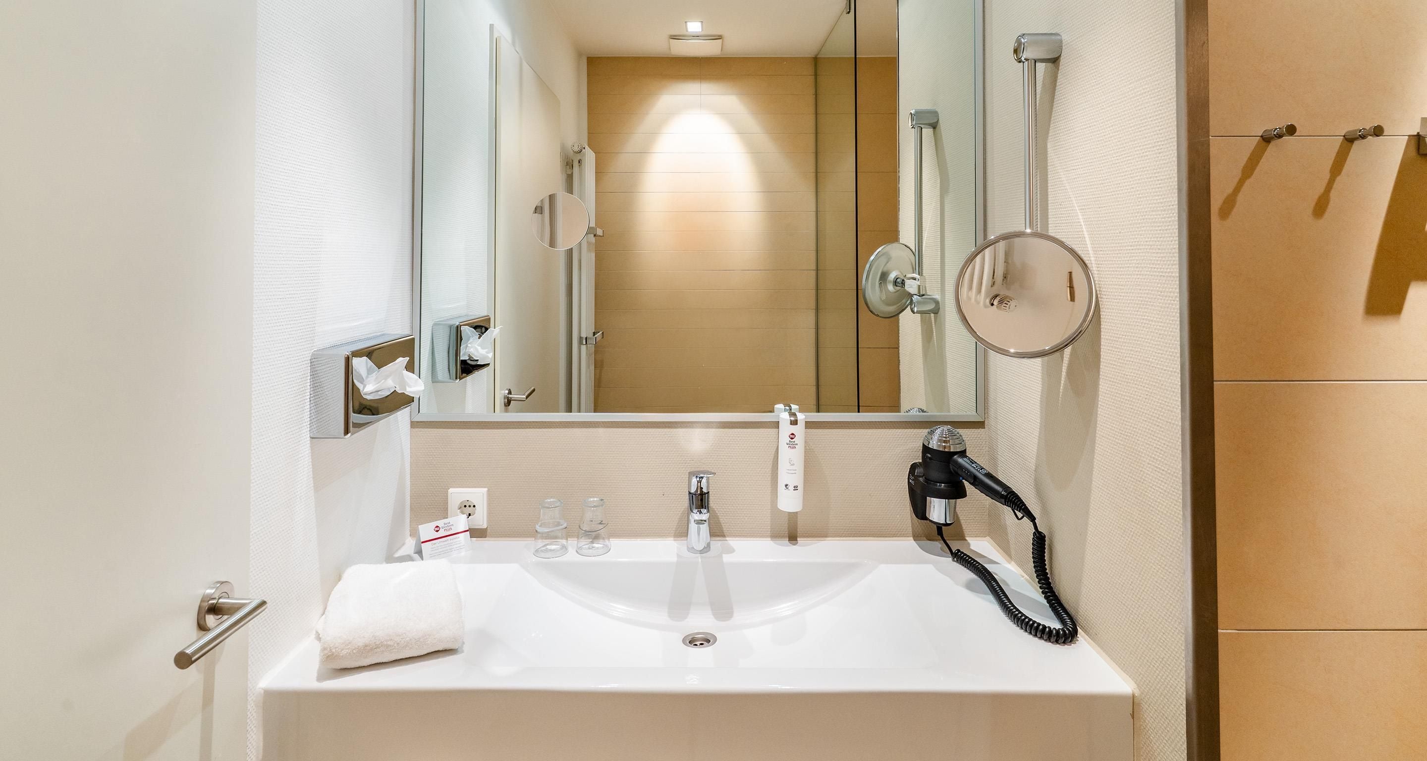 A bathroom with a white sink, a mirror, a handheld hair dryer, and a towel.