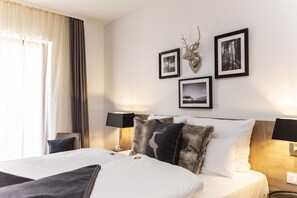 Habitación de hotel con cama, dos lámparas de noche, una mesita de noche, un adorno de cabeza de ciervo montado en la pared y tres cuadros enmarcados.