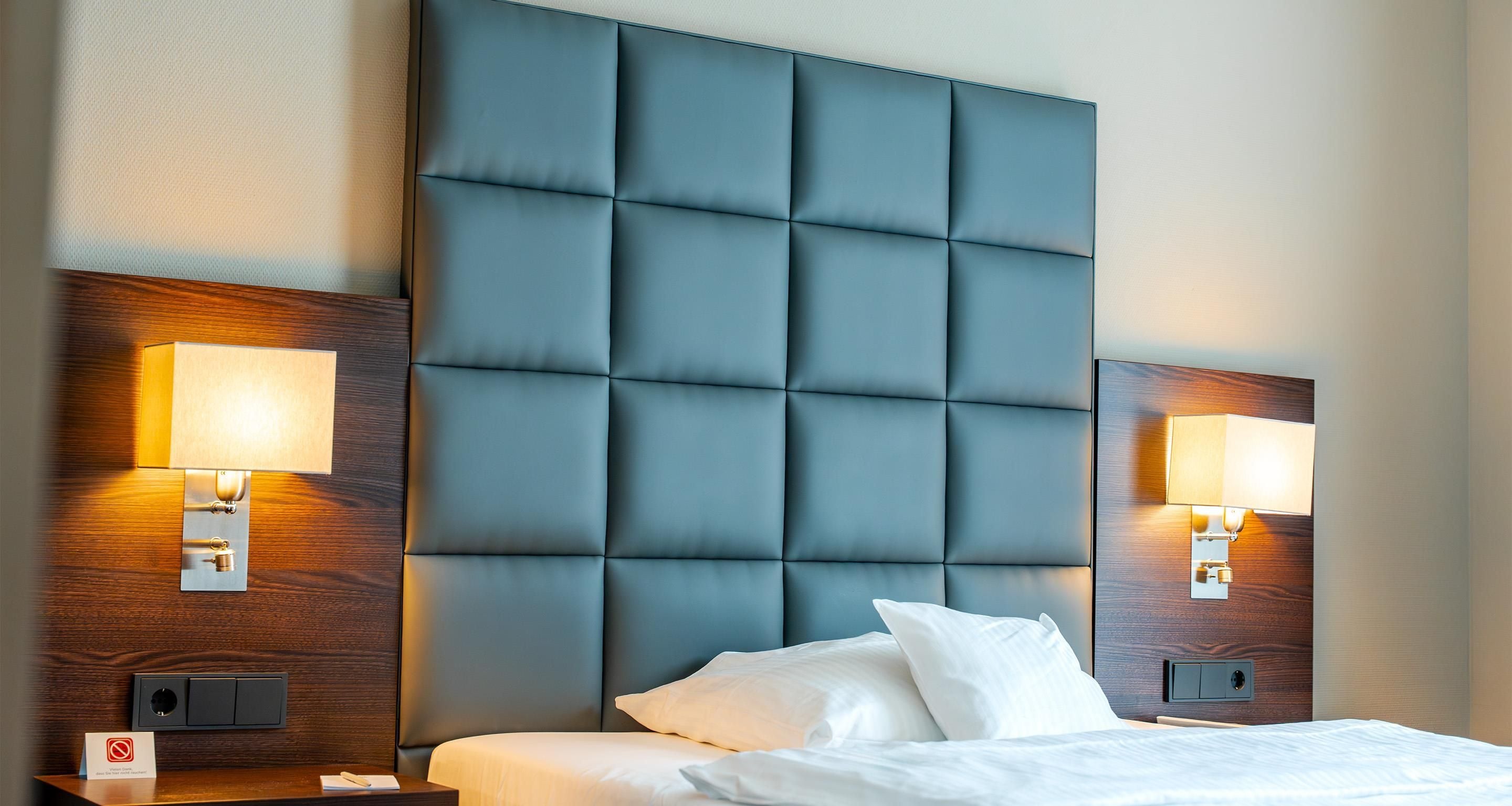 Ein Hotelzimmer mit einem großen, gesteppten Kopfteil, zwei Nachttischen mit Lampen und einem Bett mit weißen Leinentüchern.