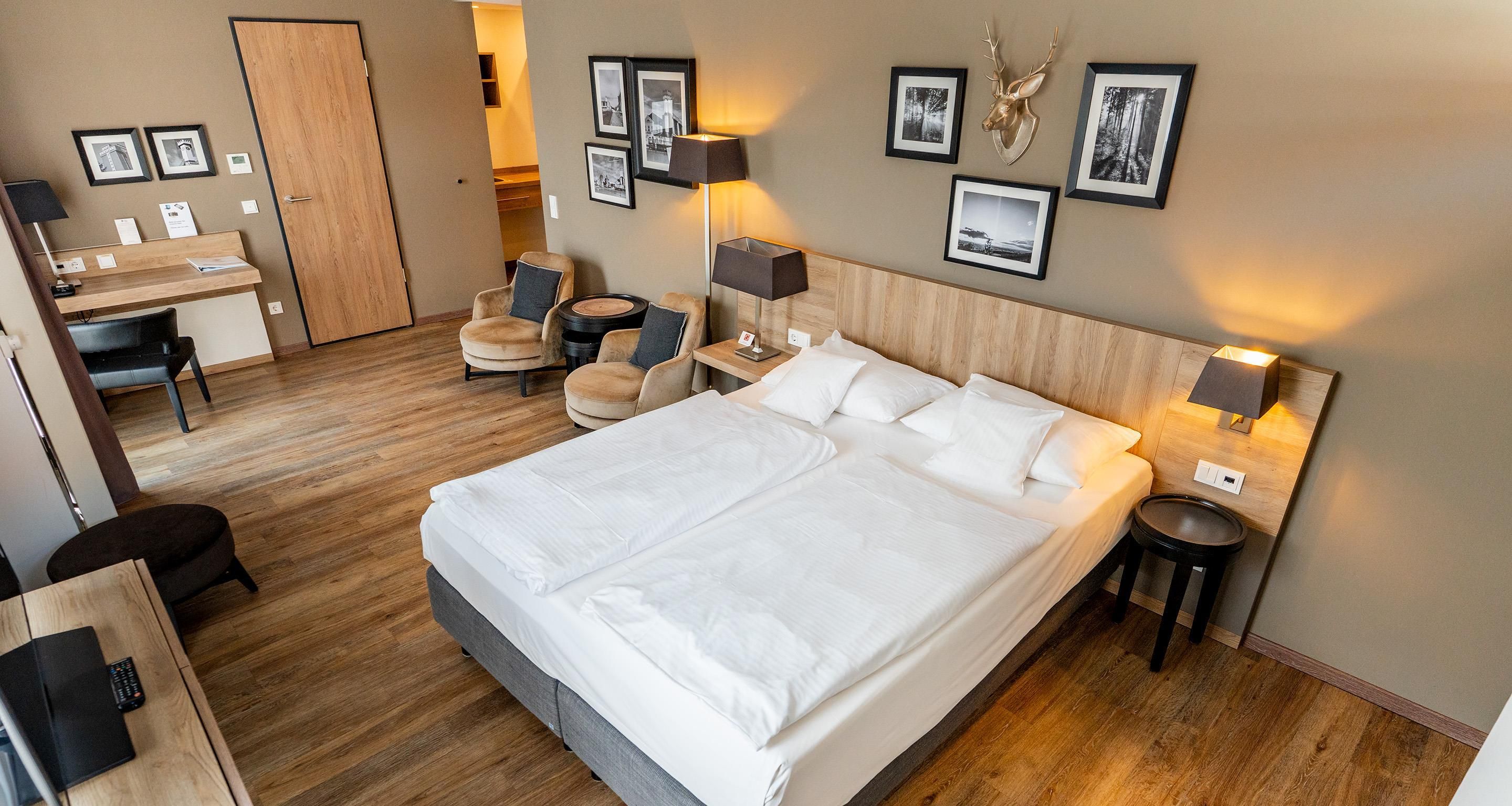 A hotel room with a large bed, a desk, a chair, a round table, and a wall with framed pictures.