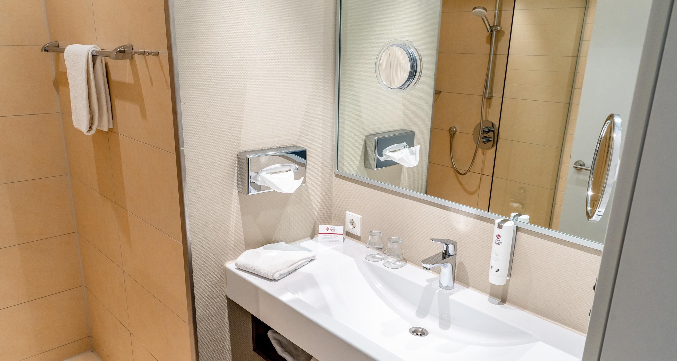 A modern bathroom with a white sink, a mirror, a towel rack, and a shower area.