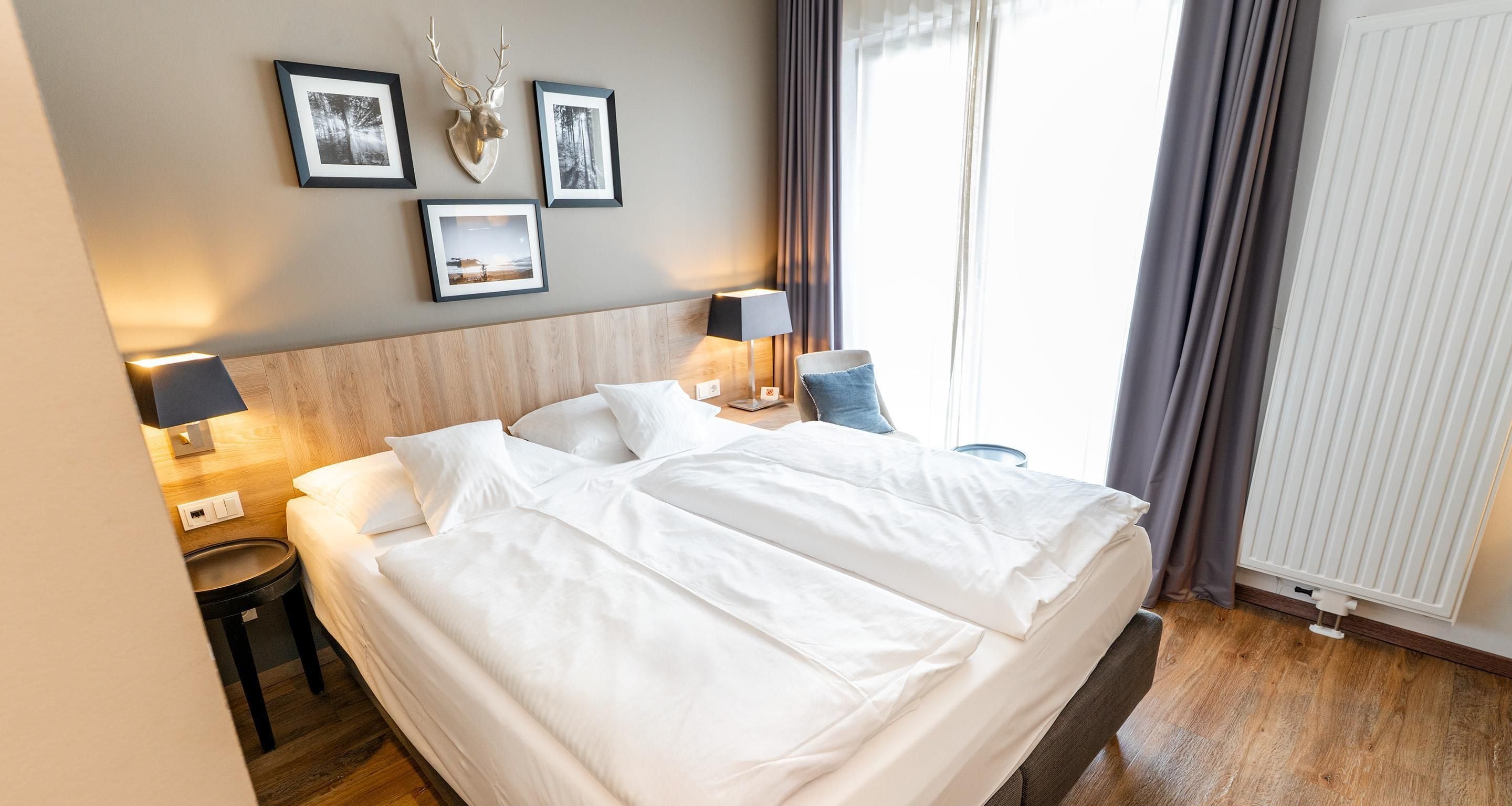 Ein Hotelzimmer mit Bett, Nachttischen, Lampen und gerahmten Bildern an der Wand.
