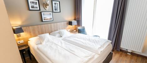 Ein Hotelzimmer mit Bett, Nachttischen, Lampen und gerahmten Bildern an der Wand.