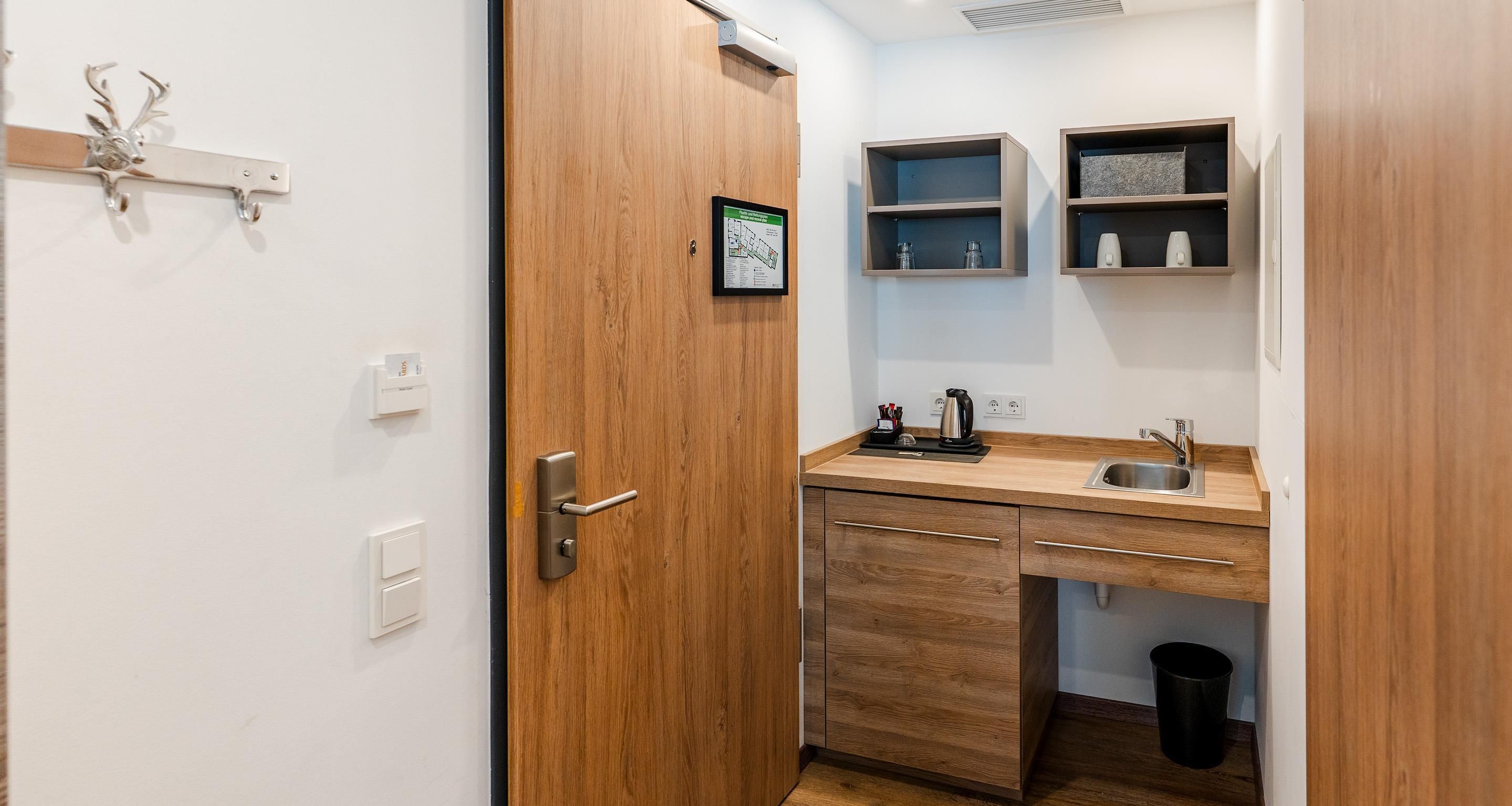 Una cocina compacta con una puerta de madera, un lavamanos y dos repisas arriba.
