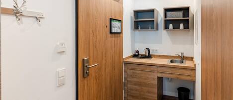 Una cocina compacta con una puerta de madera, un lavamanos y dos repisas arriba.