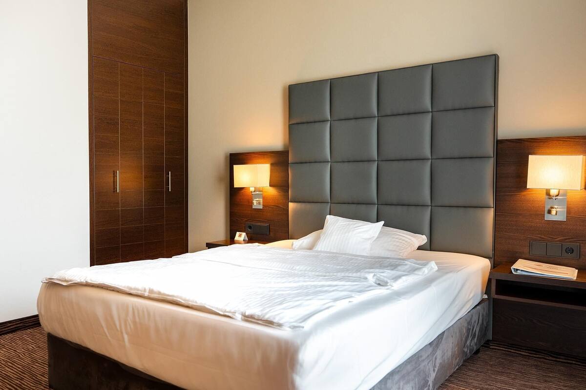 Une chambre d’hôtel avec un grand lit, une tête de lit en bois, deux tables de chevet avec des lampes et une petite table de nuit.