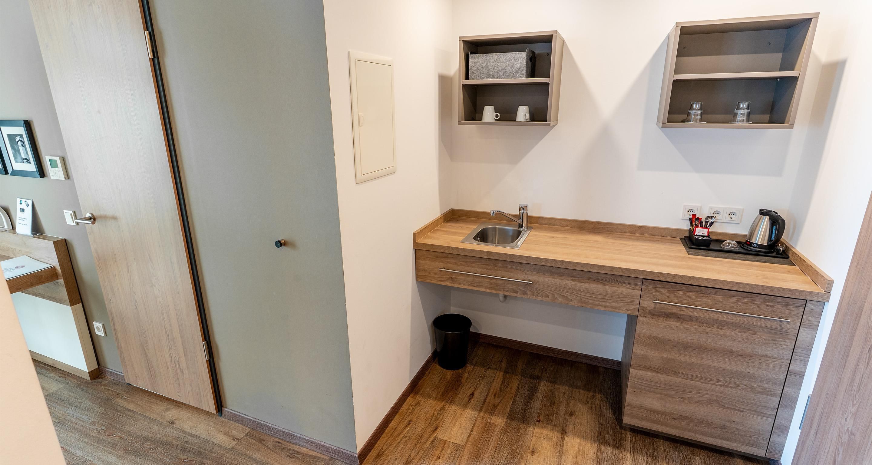 Una cocina compacta con un lavamanos, armarios de madera y una encimera. Hay dos repisas en la pared sobre el lavamanos.