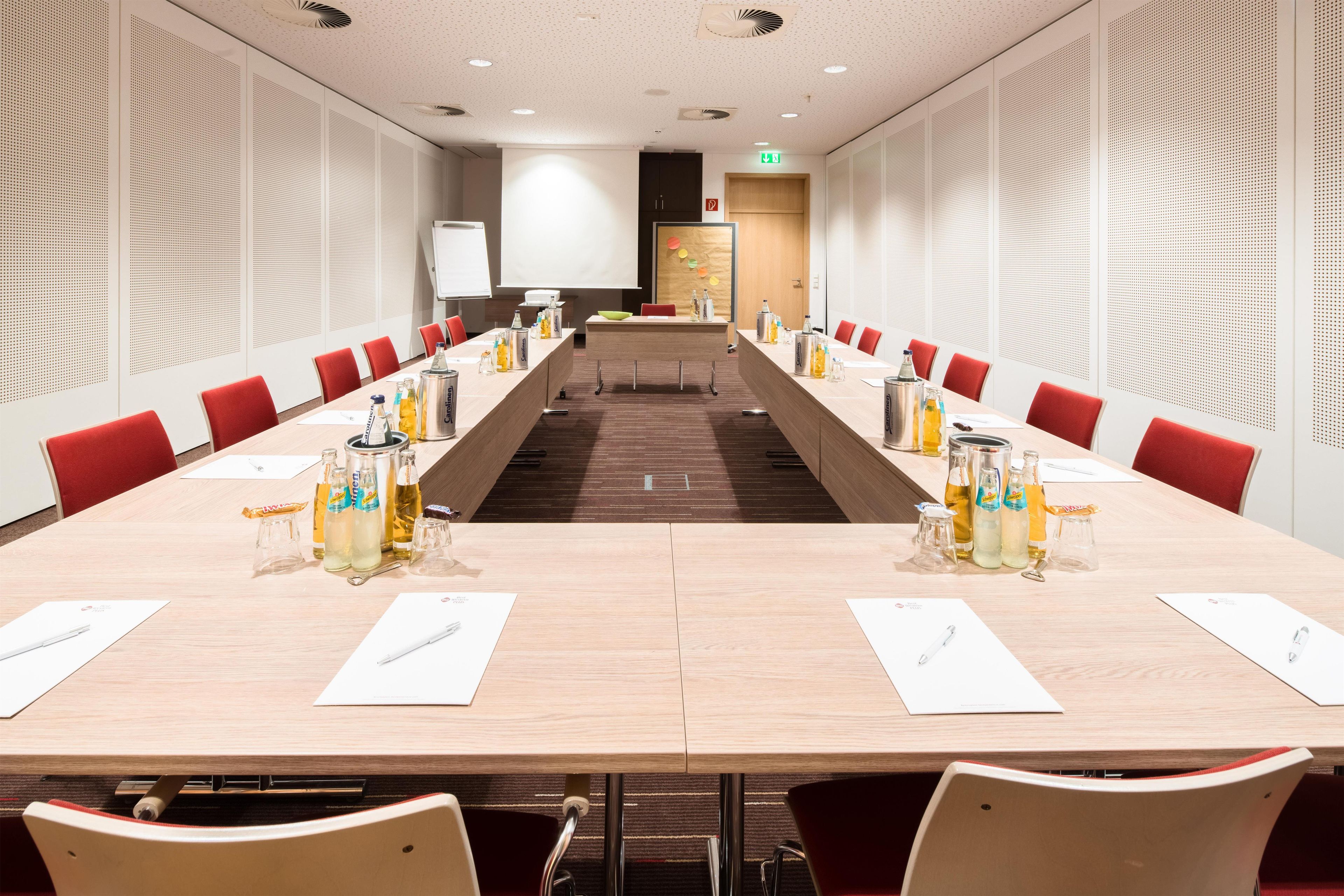 Ein Konferenzraum mit einem langen Tisch, roten Stühlen und verschiedenen Getränken.