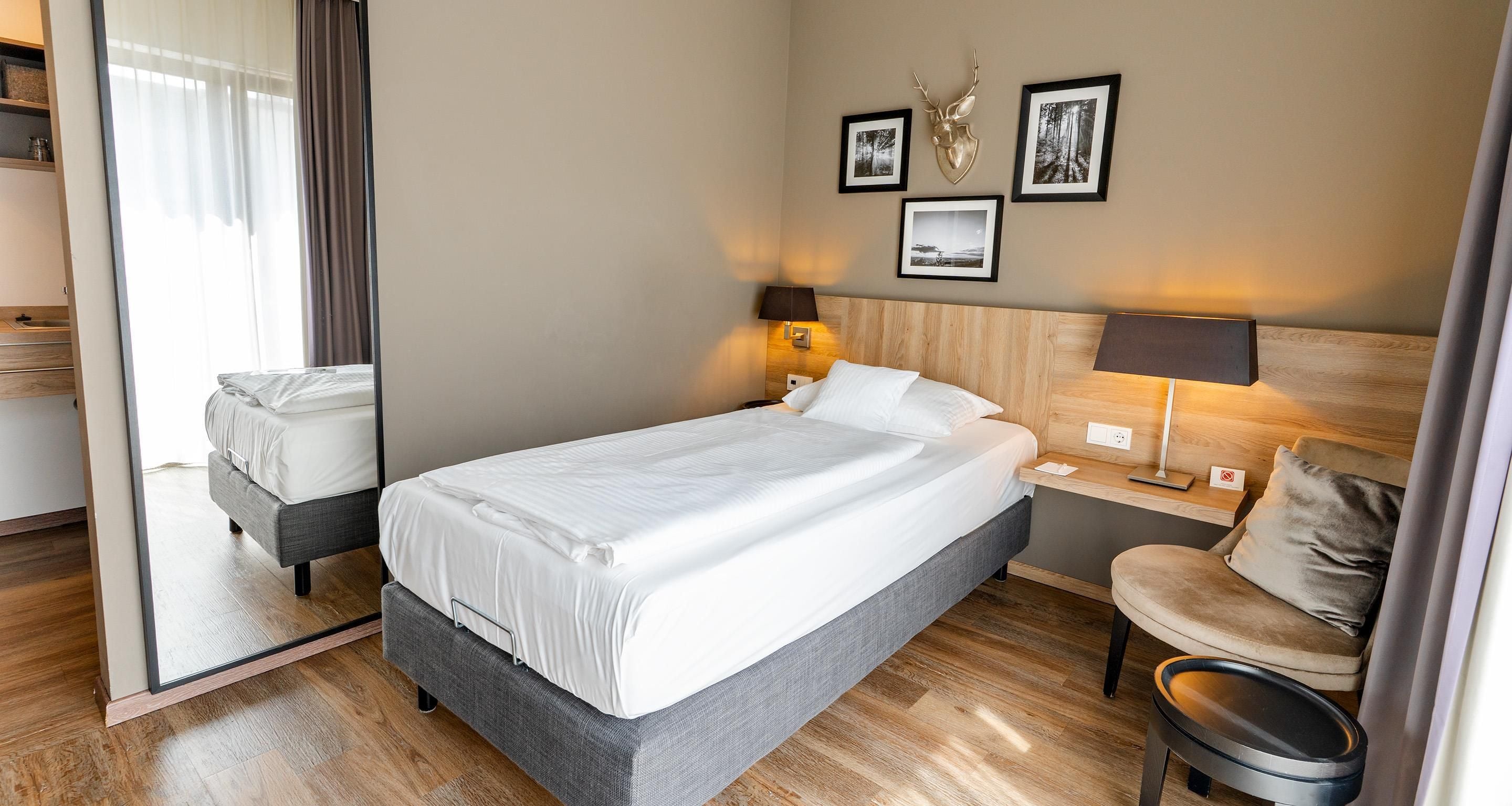 A hotel room with a bed, bedside table, lamp, chair, and a mirror.