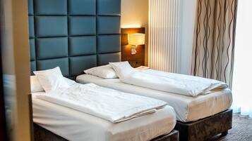 A hotel room with two beds, a padded headboard, a bedside lamp, and a window with curtains.