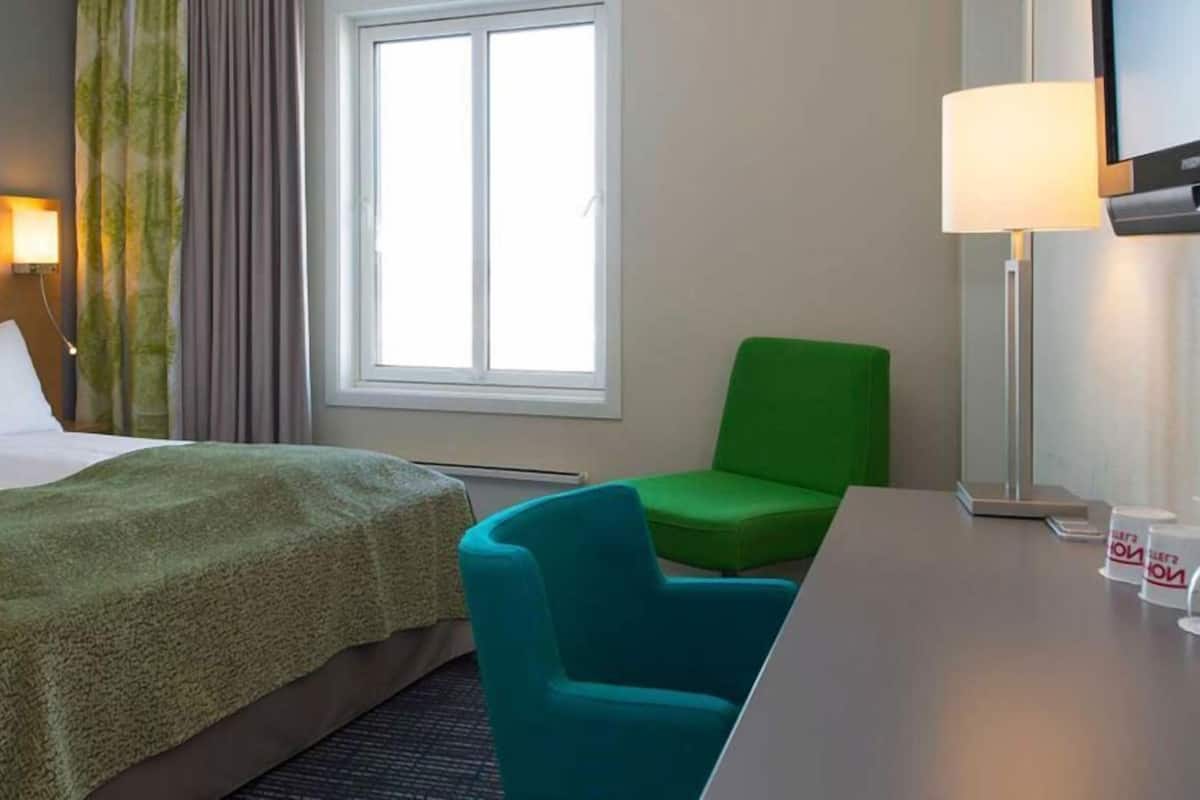 Een hotelkamer met een bed, een groene stoel, een bureau en een televisie.