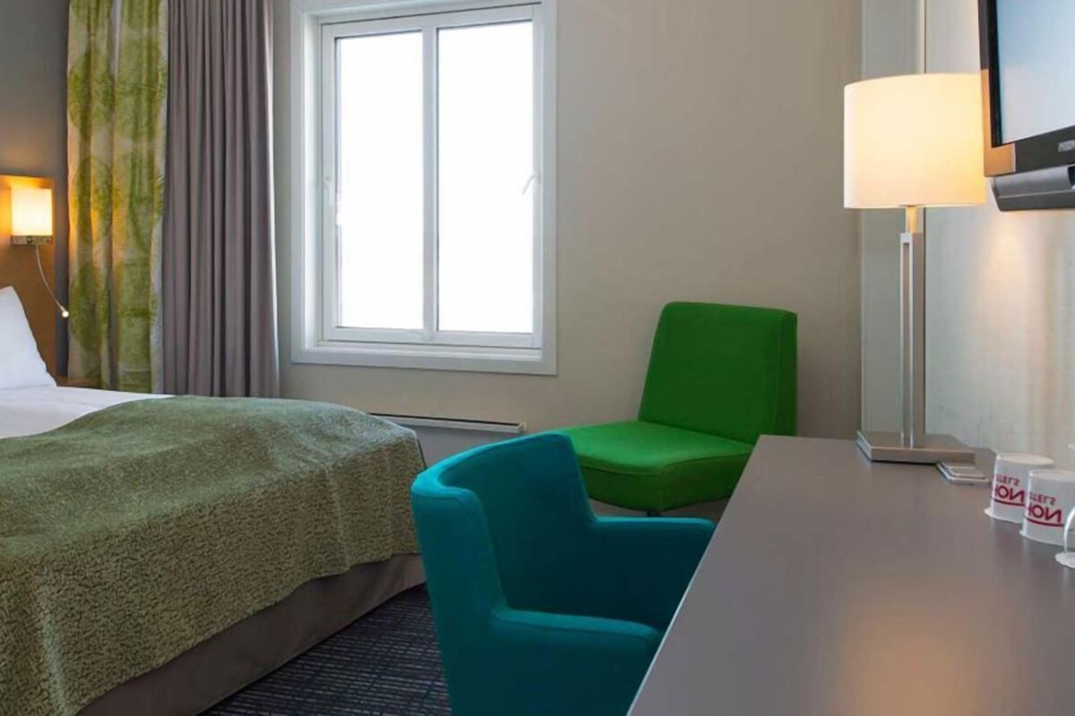 Una habitación de hotel con una cama, un sillón verde, un escritorio y un televisor.