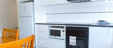 Una cocina con armarios blancos, microondas, horno y refrigerador.