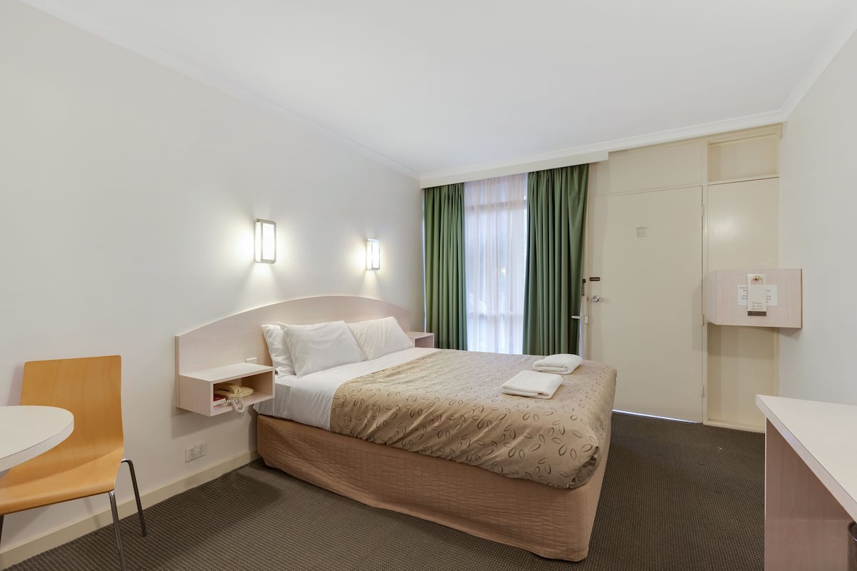 A hotel room with a bed, a chair, a desk, and a wardrobe.