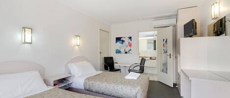 A hotel room with two beds, a desk, a chair, a TV, and a bathroom.