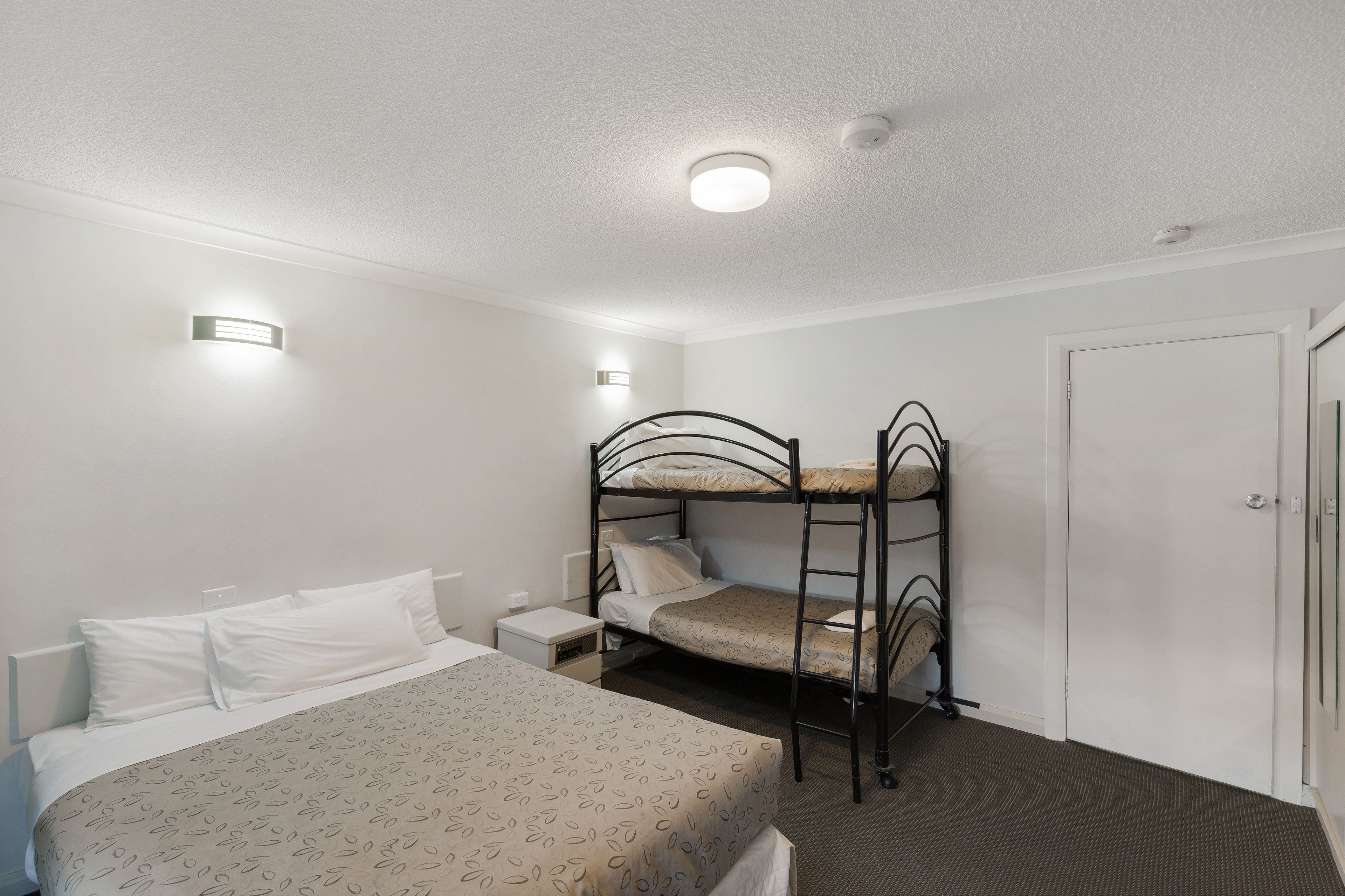 Habitación individual con literas, una mesita de noche y una puerta.