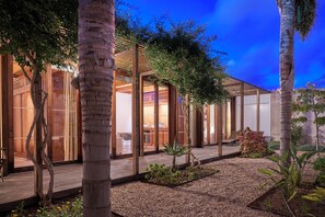 A modern building with large glass windows, a wooden deck, and a garden area with plants and gravel. - Hotel Porto Santo & Spa (Porto Santo)
