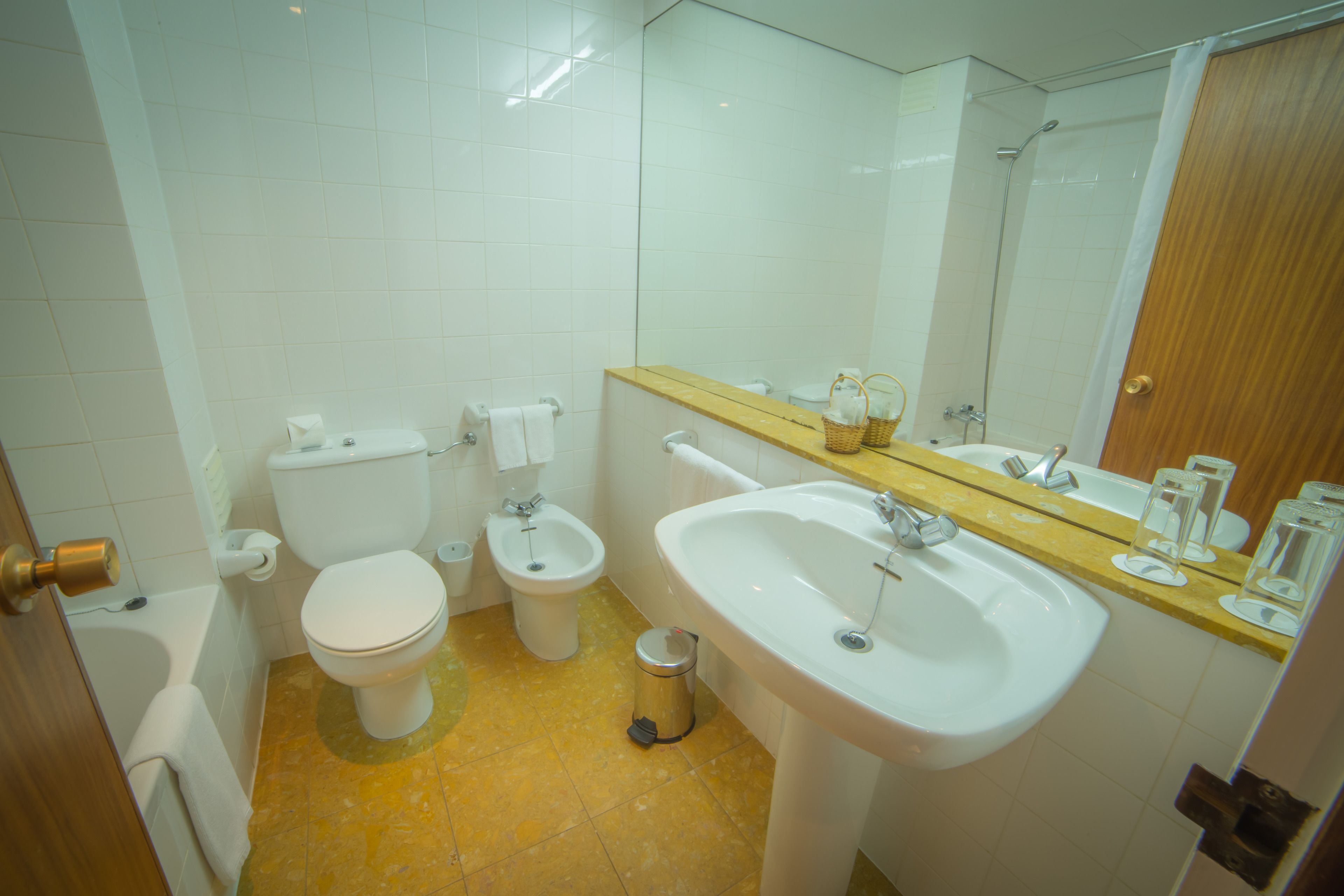 A bathroom with a toilet, bidet, sink, and a trash can.