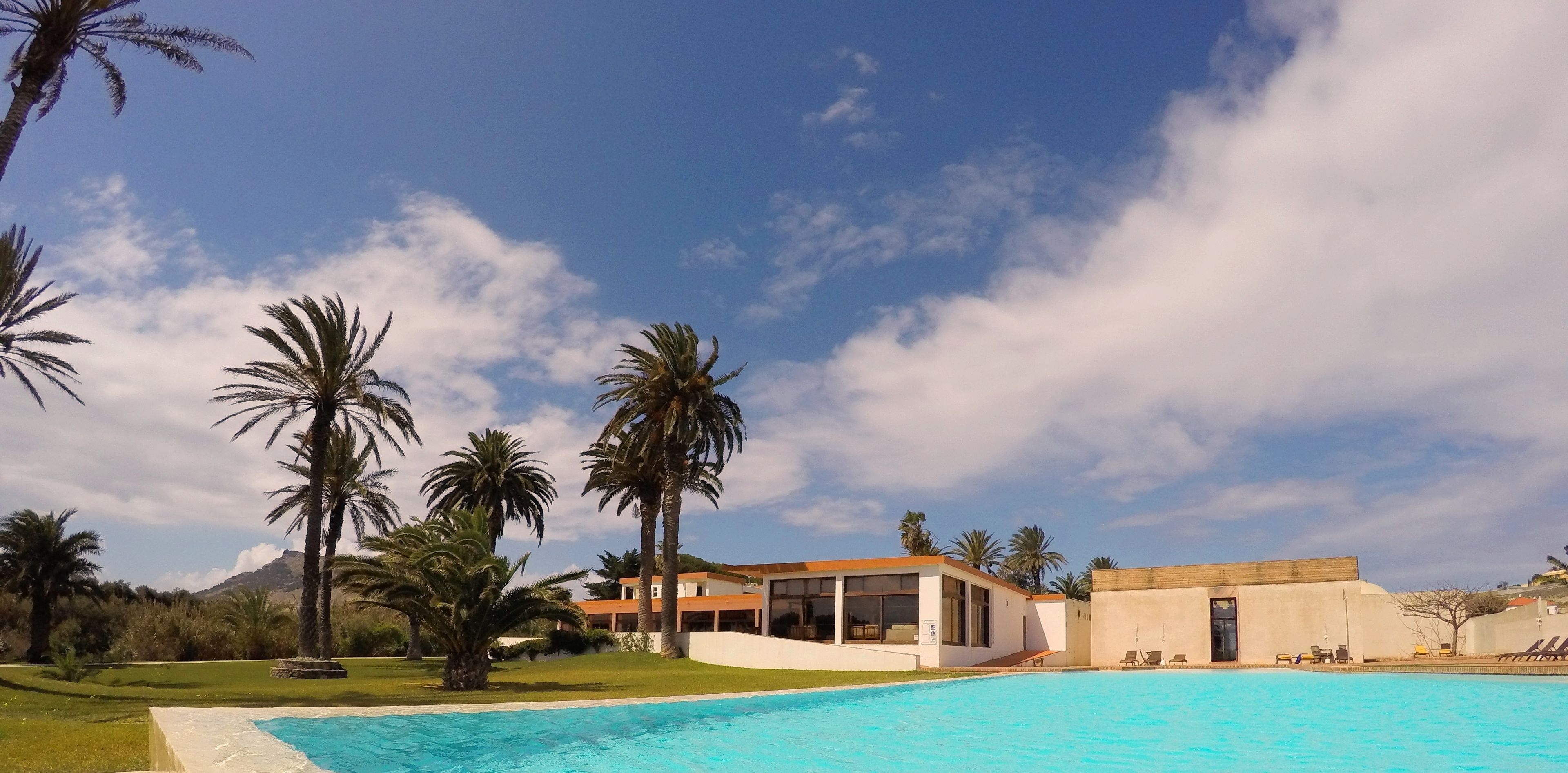 Un resort moderno con piscina, palmeras y una montaña al fondo.