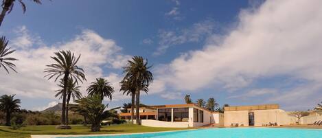 Un resort moderno con piscina, palmeras y una montaña al fondo.