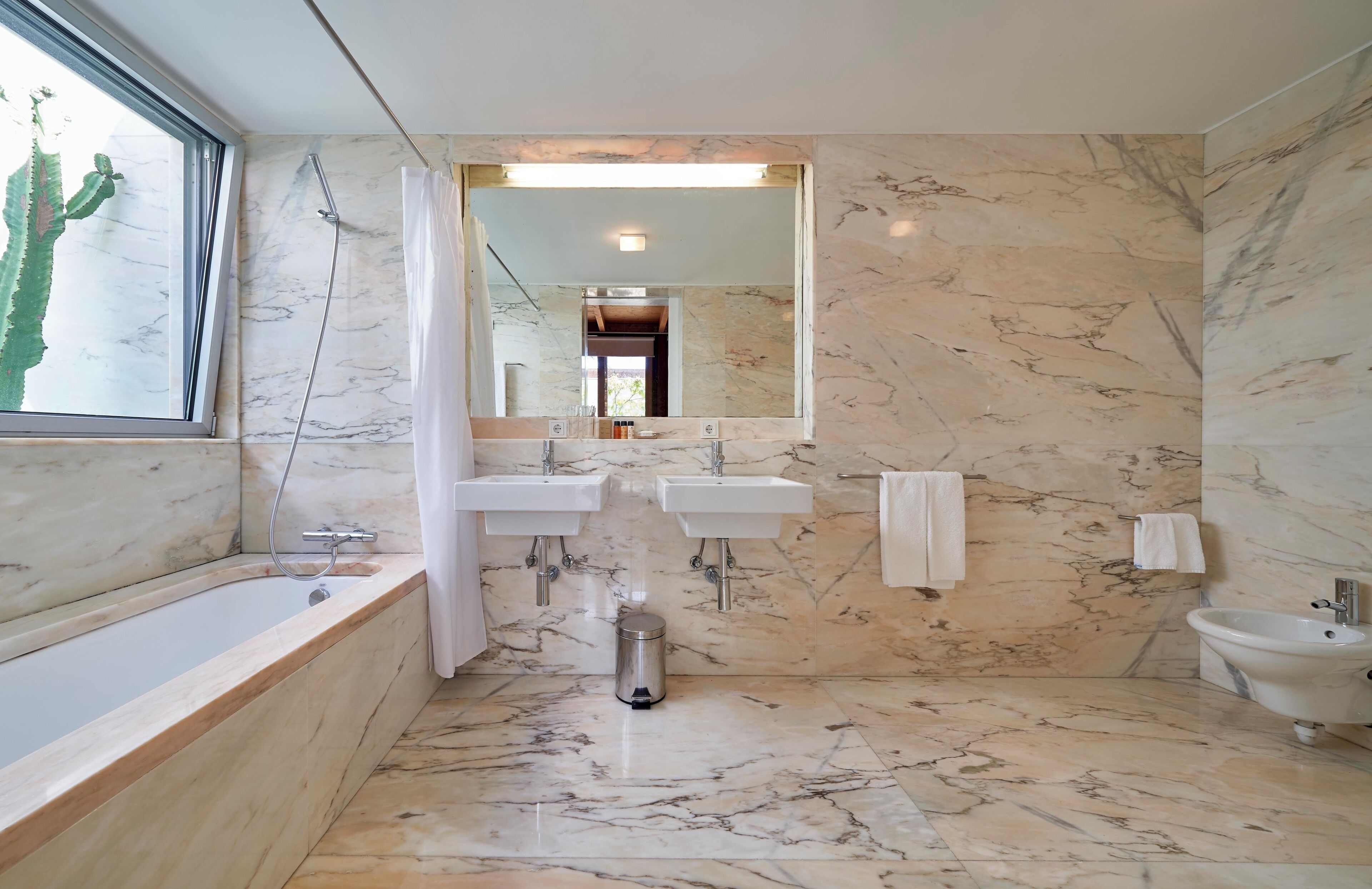 Un baño con bañera, dos lavamanos, un bidé y un espejo grande.